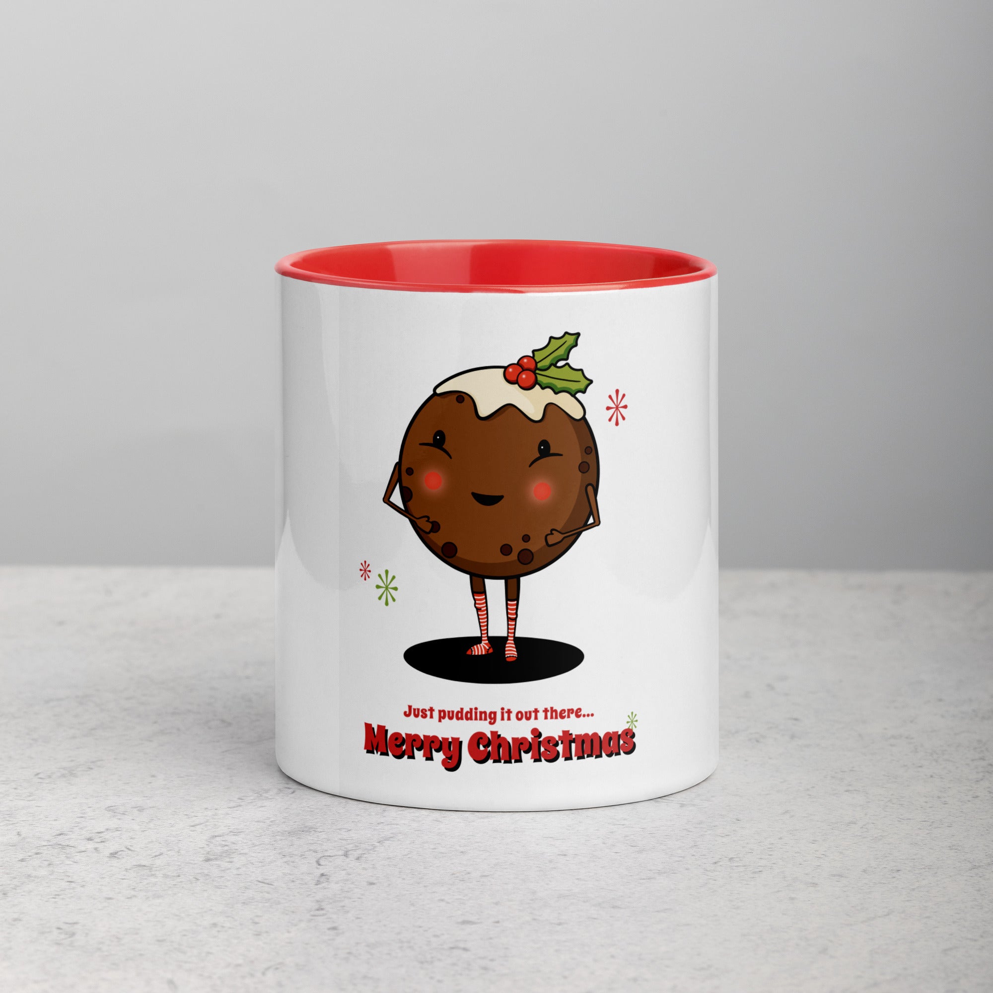 front facing white mug with red interior and handle. Mug has illustration of cute Christmas Pudding character with a custard and Christmas holly hat wearing red and white striped socks with the text Just Pudding it Out there - Merry Christmas